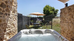Un jacuzzi en un área exterior con paredes de piedra, una mesa y sillas bajo una sombrilla.
