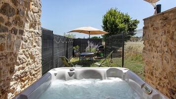 Een bubbelbad in een openluchtgebied met stenen muren, een tafel en stoelen onder een parasol.