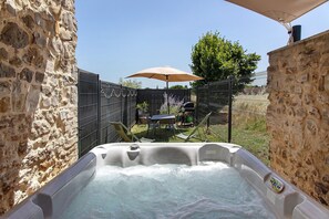 Ein Whirlpool in einer von Steinmauern umgebenen Außenanlage mit Tisch und Stühlen unter einem Sonnenschirm.