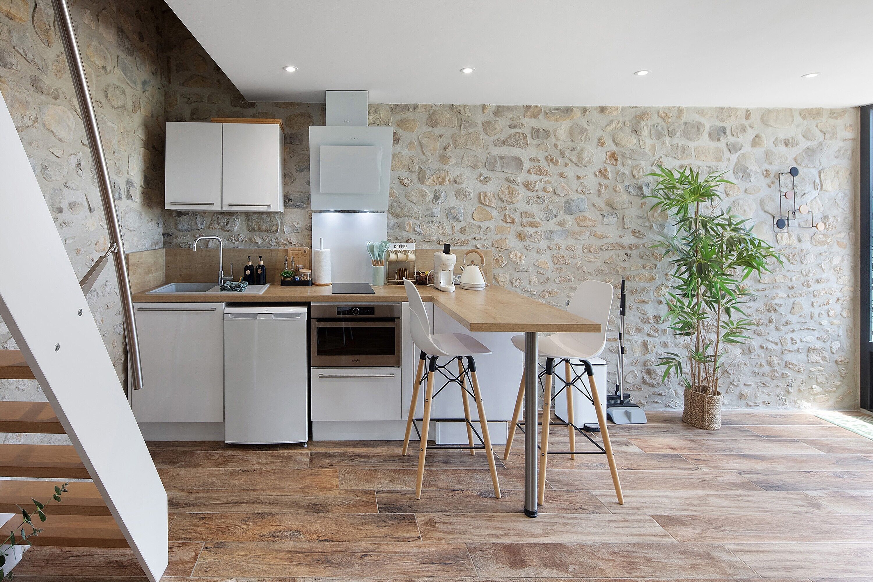 Een moderne keuken met witte kasten, een houten eettafel en een stenen wand.
