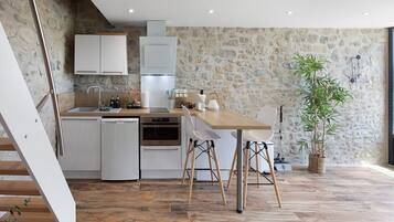 Een moderne keuken met witte kasten, een houten eettafel en een stenen wand.