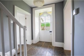 A hallway with a white door, a white railing, and a tiled floor.