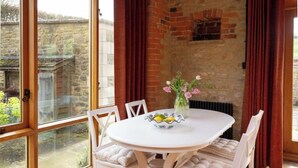 A round table with chairs, a vase with flowers, and a bowl of fruit. - Cosy Cotswold Farm Cottage – Rural Views, Charm & Peaceful Escape (Whichford)