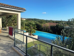 Vista da piscina com céu azul límpido, uma palmeira e um telhado telhado.