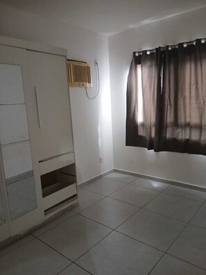 Una habitación con armario, ventana con cortinas y suelo de baldosas.