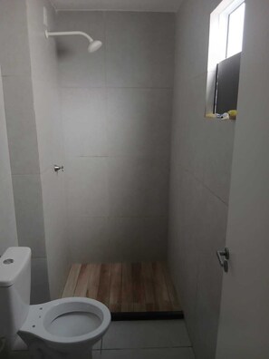 Un espacio de ducha pequeño y cerrado, con un inodoro y suelo de madera.