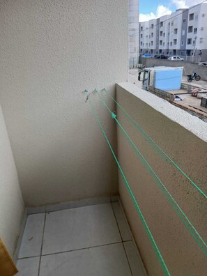 Un balcón con suelo de baldosas, pared color beige y vista a un edificio de varios pisos al fondo.