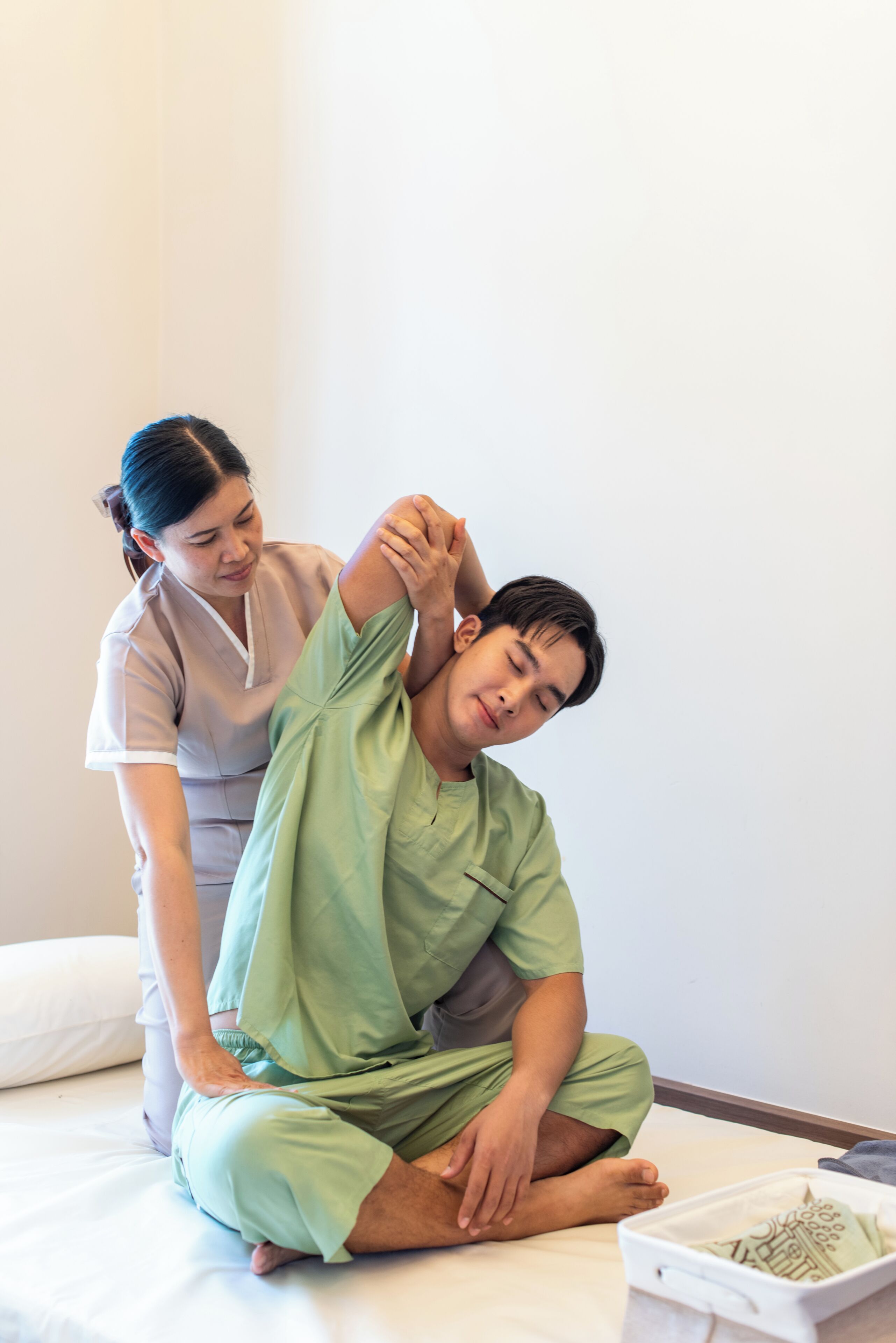 A person receiving a physical therapy session on a bed in a room with a plain wall and a white pillow.