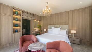 Une chambre moderne avec un grand lit, deux fauteuils, une petite table, un lustre et des étagères intégrées ornées d’objets décoratifs.