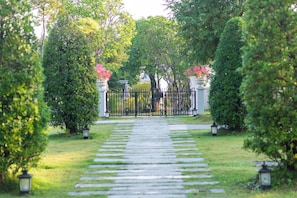 A stone pathway leading to a gated entrance surrounded by lush greenery and decorative lanterns. - Kaysorn Siri (Sirindhorn)
