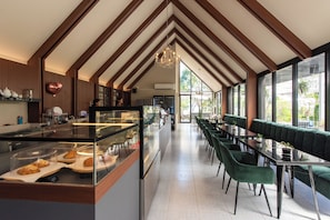 A modern restaurant with a long counter, green upholstered seating, and large windows. - Kaysorn Siri (Sirindhorn)
