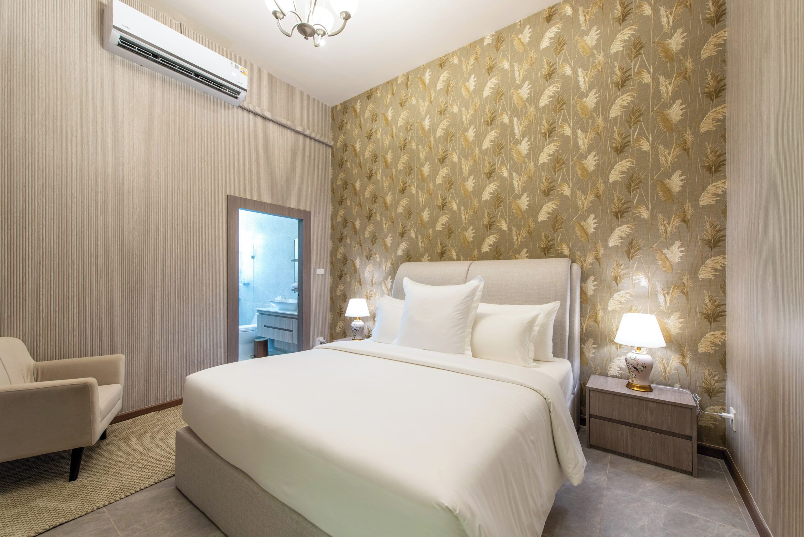 A hotel room with a large bed, two bedside tables with lamps, a chair, and an air conditioning unit.