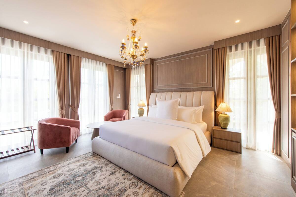 Un dormitorio espacioso con una cama grande, una zona de estar con una silla, una mesita y una mesita de noche con lámpara.