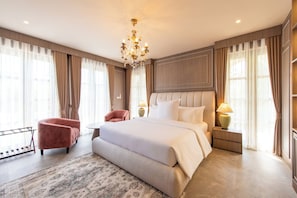 A spacious bedroom with a large bed, a sitting area with a chair, a small table, and a nightstand with a lamp. - Kaysorn Siri (Sirindhorn)