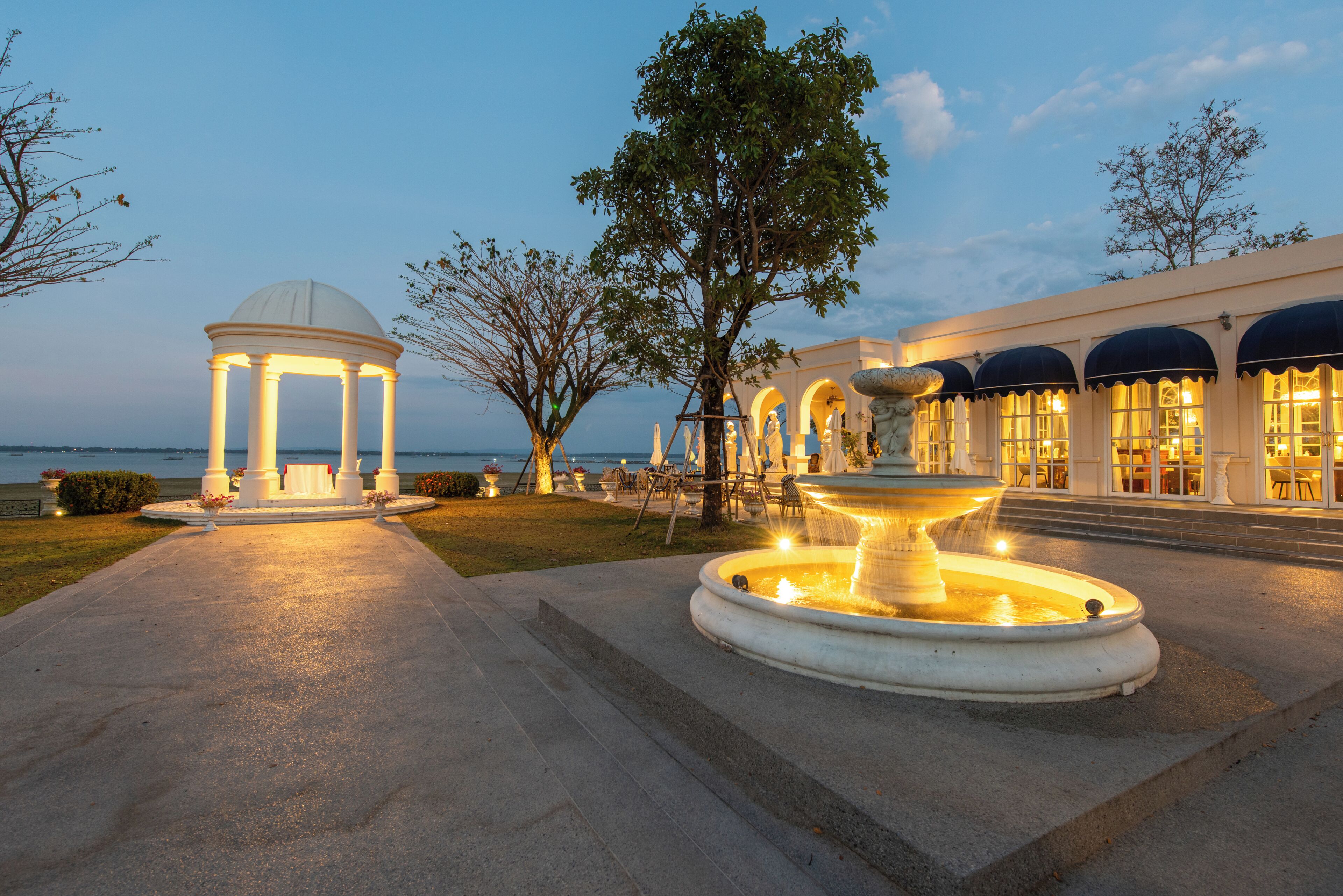 A well-lit outdoor area with a fountain, a gazebo, and a building with arched windows.