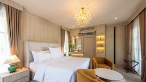 Habitación de hotel con una cama grande, zona de estar con una mesa y sillas, un candelabro y un espejo sobre la cama.