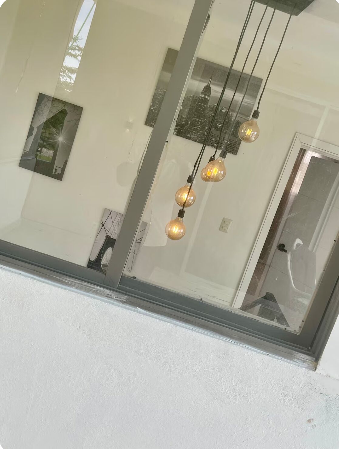 Una stanza con un'ampia finestra, un lampadario con tre luci e un quadro appeso al muro.