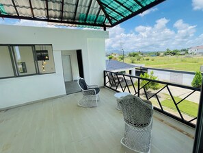 A balcony with two wicker chairs, a table, and a view of a green landscape.