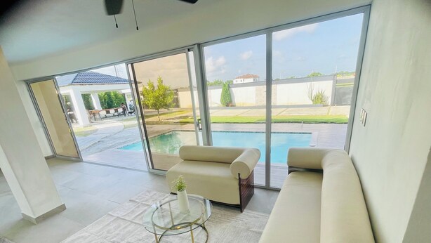 A modern living room with a large glass door leading to a pool area, a beige sofa, and a glass coffee table. - Marvelous 3-bedroom house with AC in charming in Bani, Pizarrete (Pizarrete)