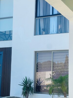 A multi-story building with large windows, a blue door, and potted plants.
