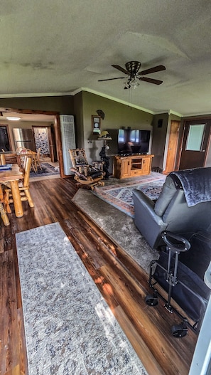 A living room with a sofa, a TV, a ceiling fan, and a dining area with chairs and a table. - Bell Inn Cottage - Sanford Lake (Sanford)