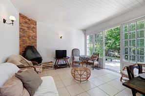 Un salon doté d’une cheminée, d’un téléviseur, de meubles en osier et de grandes fenêtres.