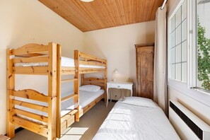 A bunk bed room with a wooden ceiling, a desk, and a window with a view.