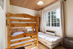 Une chambre avec un lit superposé, un lit simple, un bureau et une fenêtre avec des rideaux.