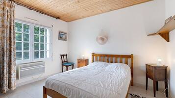 Ein Schlafzimmer mit Holzboden, einem Bett, einem Sessel, einem Nachttisch, einem Heizkörper und einem Fenster mit Vorhängen.