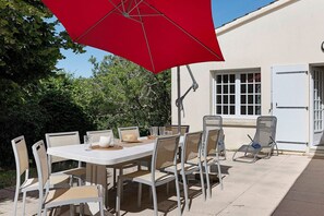 An outdoor dining area with a table, chairs, and a red umbrella.