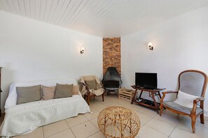 Un salon comprenant un canapé, deux fauteuils, une chaise en osier, un téléviseur et une cheminée.