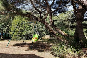 A swing set in a wooded area with a large tree nearby.