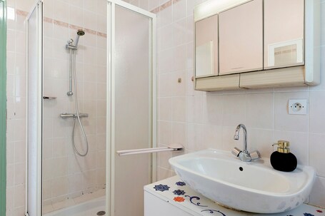 A bathroom with a shower, sink, mirror, and decorative tiles.. One Hectare Near the Ocean