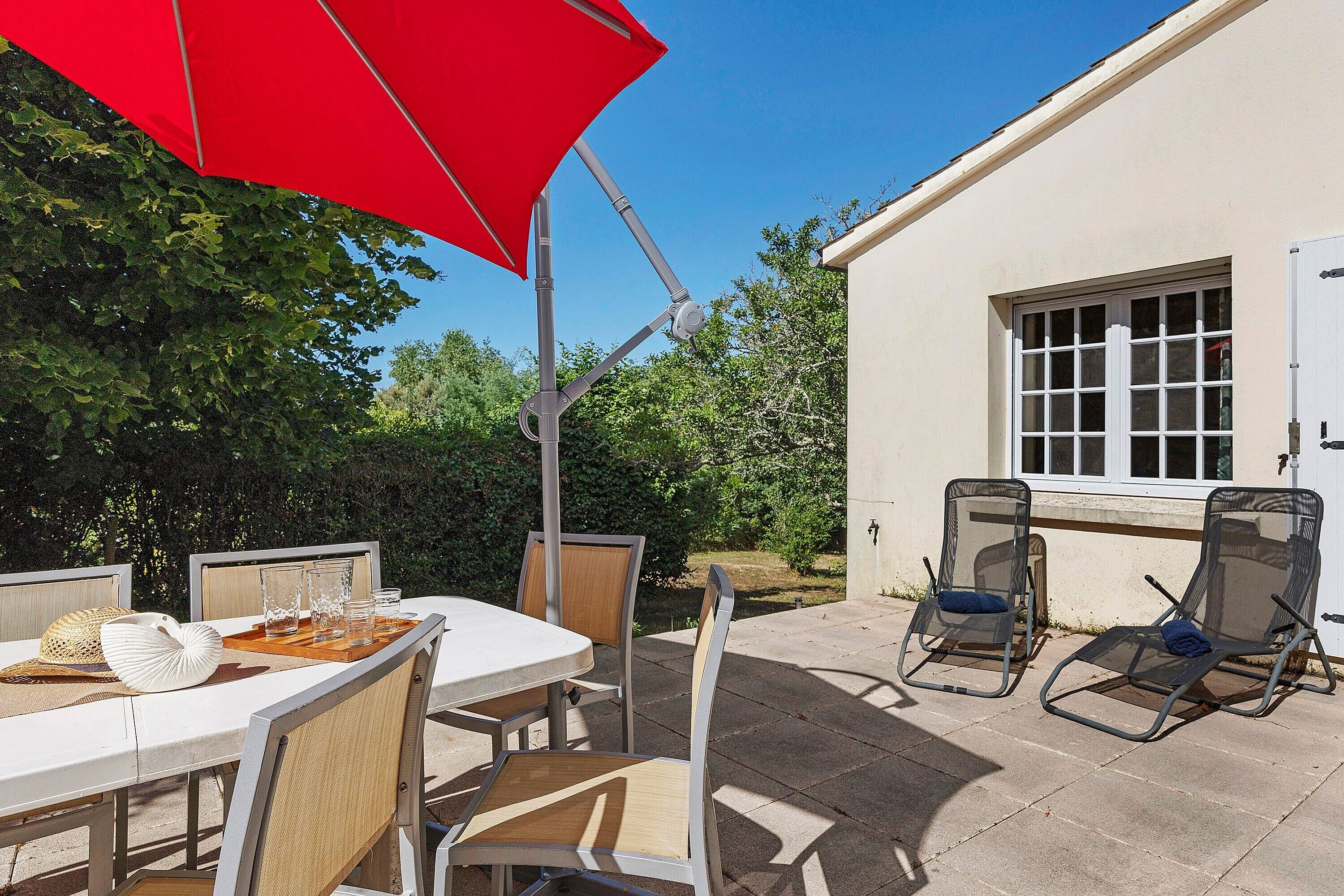 Een terras buiten met een tafel, stoelen en een rode parasol.
