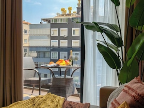 Ein Balkon mit Korbstühlen, einem Tisch mit Obst und einer Flasche sowie Blick auf Gebäude.