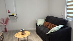 A living room with a black sofa, a round wooden table, a white radiator, and a window with blinds. - Mimi's House (Maubert-Fontaine)