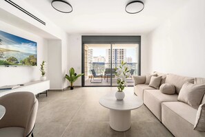 A modern living room with a sofa, a round table, a TV, and a balcony with a city view. - Modern 4BR Balcony Mamad Renovated Bldg (Bat Yam)
