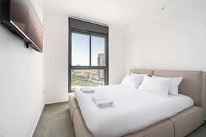 Ein modernes Hotelzimmer mit einem großen Bett, einem Fenster mit Blick auf die Stadt und einem wandmontierten Fernseher.