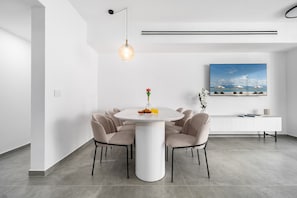 Ein moderner Essbereich mit einem runden Tisch, sechs Stühlen, einer Pendelleuchte, einem weißen Konsolentisch und einem großen gerahmten Bild an der Wand.