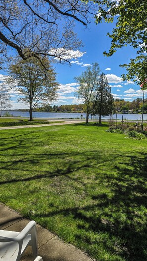 Un parque con césped, árboles, un banco y un lago al fondo.