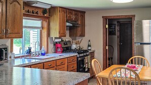 A kitchen with wooden cabinets, a granite countertop, a dining table with chairs, and a rug. - Bell Inn Cottage (Sanford)