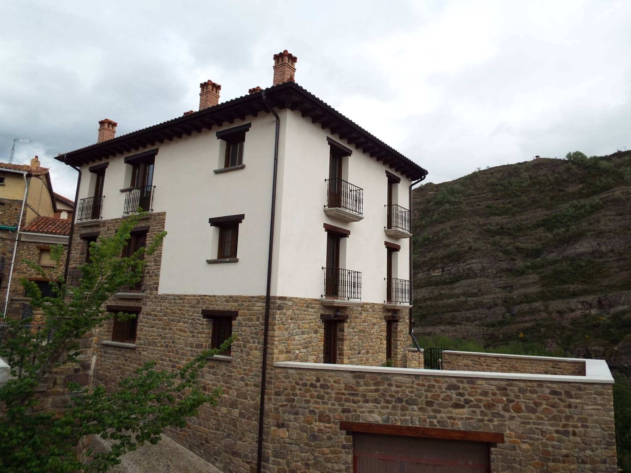 A multi-story building with stone and plaster exterior walls, multiple balconies, and a mountainous backdrop.