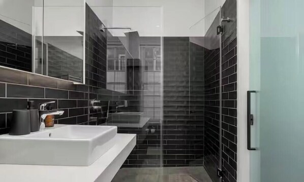 A modern bathroom with a white sink, dark tiled walls, and a glass shower enclosure. - Luxurious Holiday House With Private Pool- Cape Town City Centre (Cape Town)