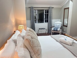 Una habitación de hotel con cama, una silla, ventana con cortinas, lámpara y espejo.
