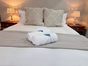 A neatly made bed with two pillows, a blanket, and two rolled towels on a textured bedspread.
