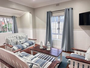 A living room with a sofa, armchairs, a coffee table, and a TV mounted on the wall.