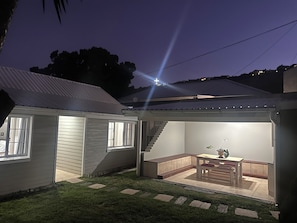 A covered outdoor area with a bench and table, a staircase, and a view of the surrounding neighborhood at dusk.