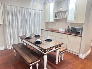 Une cuisine avec une table en bois dressée pour quatre personnes, des armoires blanches, une horloge et un four à micro-ondes.
