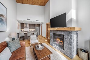 Ein modernes Wohnzimmer mit Kamin, Fernseher, einer Couch und einer Küche im Hintergrund.
