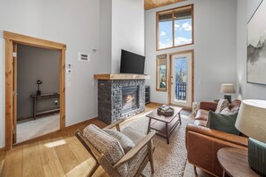 Ein Wohnzimmer mit Kamin, Holzmöbeln und Blick ins Freie.